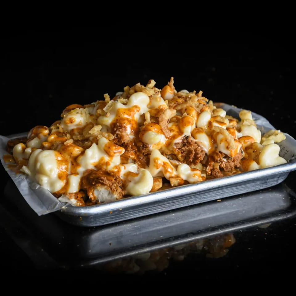 A metal tray filled with Chick N Burger's mac and cheese, chicken, fries, and orange sauce.