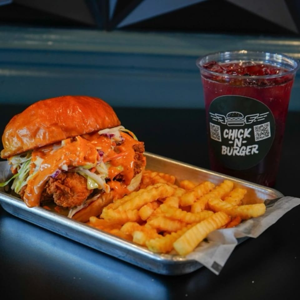 Chick N Burger's spicy chicken sandwich with coleslaw, fries, and a red drink on a metal tray.